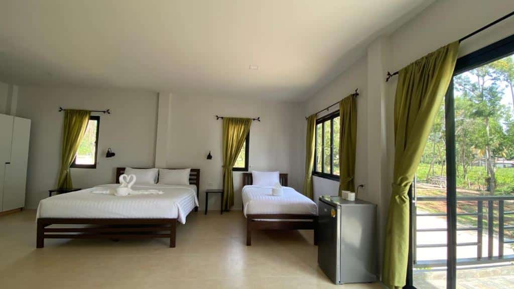 ห้องพักในโรงแรมที่สว่างสดใสและโปร่งสบายพร้อมเตียงคู่ 1 เตียงและเตียงเดี่ยว 1 เตียง มีหน้าต่างบานใหญ่พร้อมผ้าม่านสีเขียวและทิวทัศน์กลางแจ้ง ที่เที่ยวขนอม
