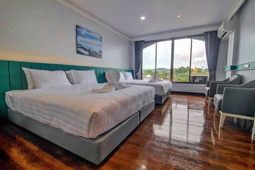 ห้องพักในโรงแรมสว่างและสะอาดพร้อมเตียงคู่ขนาดใหญ่ เตียงเดี่ยวเสริม พื้นไม้มันเงา และวิวภายนอกผ่านหน้าต่าง 2 บาน ที่พักเบตง