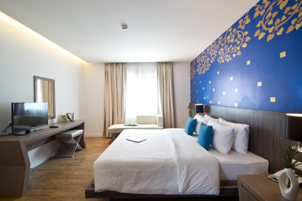 ห้องพักในโรงแรมทันสมัยพร้อมเตียงแฝด หัวเตียงสีฟ้าตกแต่ง และทีวีจอแบนบนโต๊ะที่จอมเทียน ที่พักหาดจอมเทียน