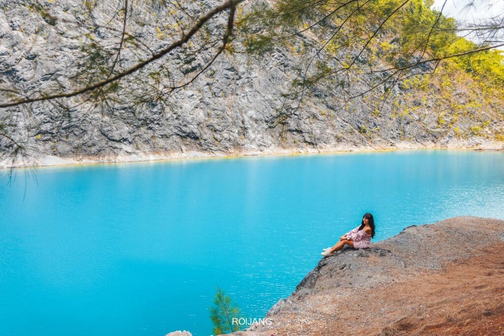 คนนั่งอยู่บนโขดหินริมทะเลสาบสีฟ้าอันเงียบสงบ รายล้อมไปด้วยหน้าผาสูงชันที่เที่ยวพังงา