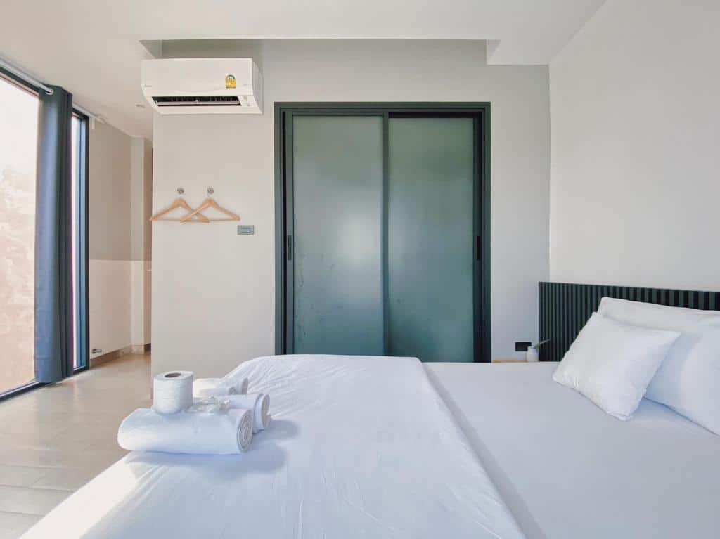 ห้องพักในโรงแรมสไตล์มินิมอลที่จัดเตรียมไว้อย่างประณีตพร้อมชุดเครื่องนอนสีขาว ผ้าเช็ดตัวบนเตียง และประตูบานเลื่อน ที่พักเบตง โรงแรมในเบตง