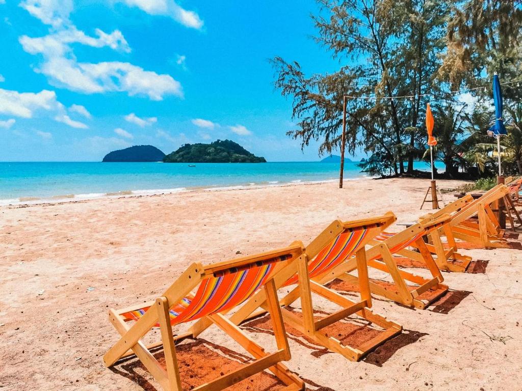 เก้าอี้ชายหาดหลากสีสันเรียงรายหันหน้าไปทางทะเลในเขตร้อนที่มีแสงแดดสดใสโดยมีเกาะหมากอยู่ไกลออกไป ที่พักเกาะหมาก