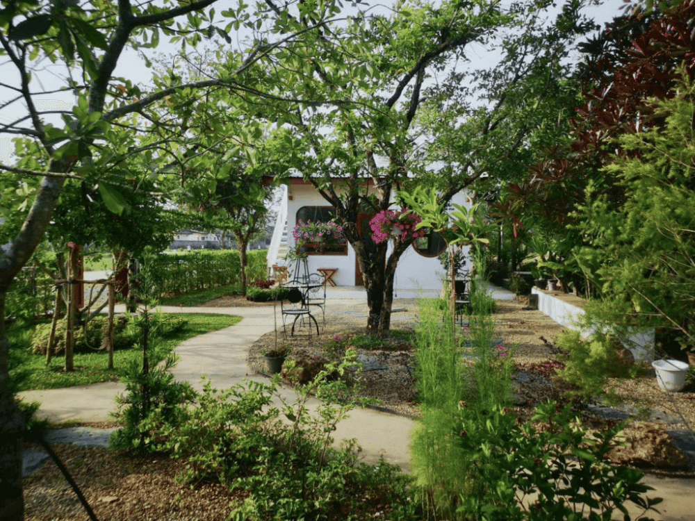 สวนอันเงียบสงบพร้อมทางเดินไปสู่กระท่อมสีขาว ล้อมรอบด้วยแมกไม้เขียวขจีและไม้ดอกใกล้ ตลาดบ้านเพ
