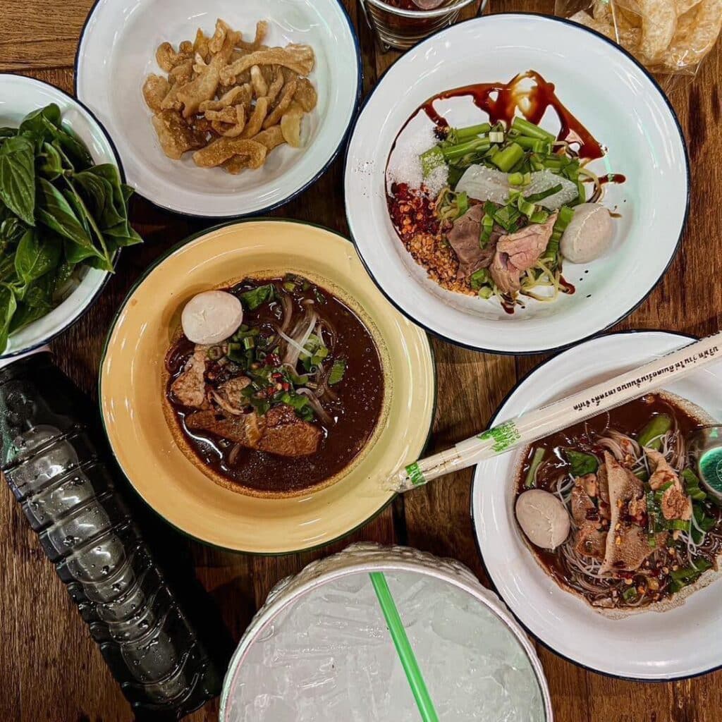 อาหารไทยนานาชนิดบนโต๊ะไม้ที่ตลาดนัดเลียบด่วนรามอินทรา รวมทั้งชามซุปก๋วยเตี๋ยว เอเชียทีคดิสนีย์