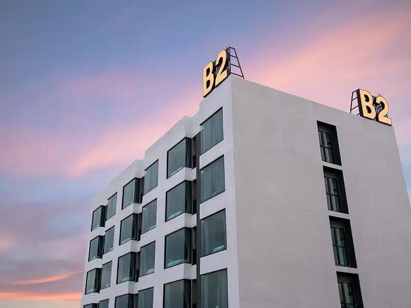 อาคารโรงแรมทันสมัยยามพลบค่ำพร้อมป้าย "b2" บนดาดฟ้าตัดกับท้องฟ้าสีชมพูและสีฟ้าในภาษามุกดาหารริมโขง ที่พักริมโขงมุกดาหาร