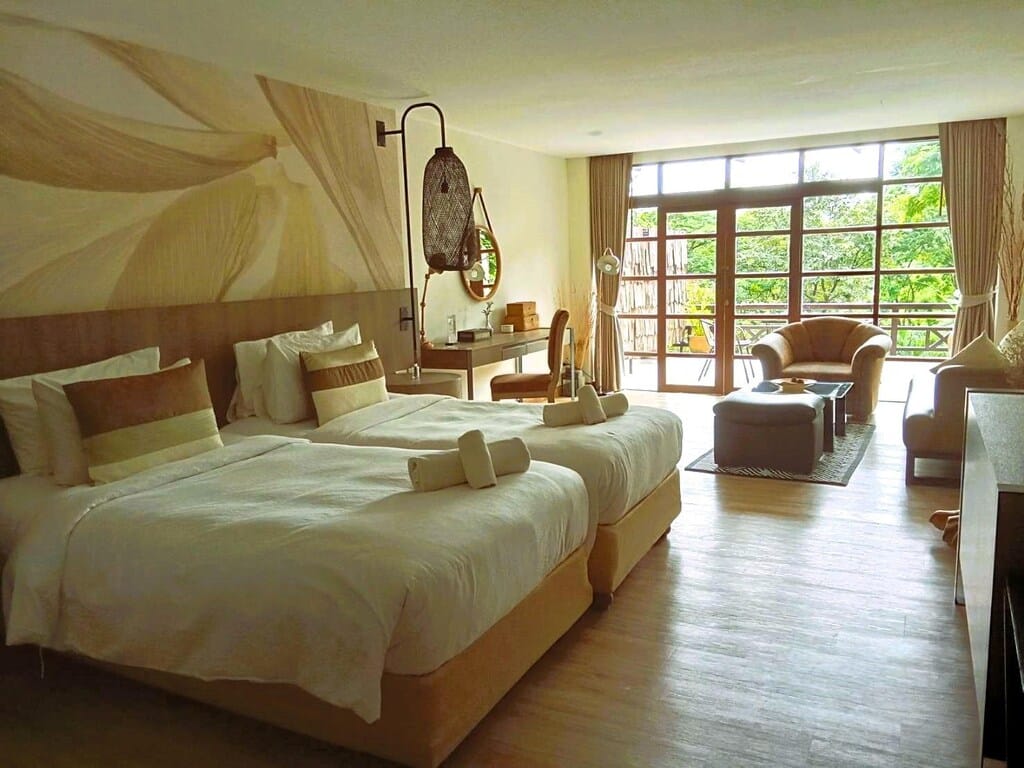 ห้องพักในโรงแรมสว่างสดใสพร้อมเตียง 2 เตียง พื้นที่นั่งเล่น และหน้าต่างบานใหญ่พร้อมวิวสวน รีสอร์ทมวกเหล็ก