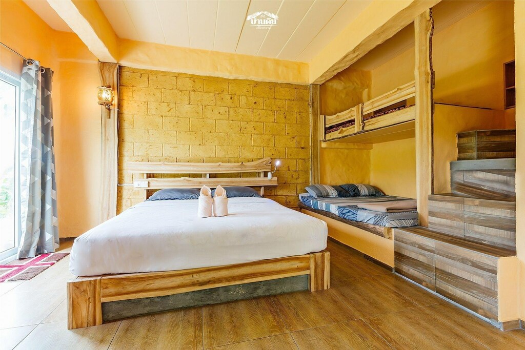ห้องนอนแสนสบายที่มีแสงสว่างอบอุ่นและมีเตียงคู่ขนาดใหญ่อยู่ตรงกลาง เตียงสองชั้นทางด้านขวา และพื้นไม้ธรรมชาติ พร้อมด้วยองค์ประกอบของการตกแต่งแบบเรียบง่าย ที่พักเขื่อนเชี่ยวหลาน