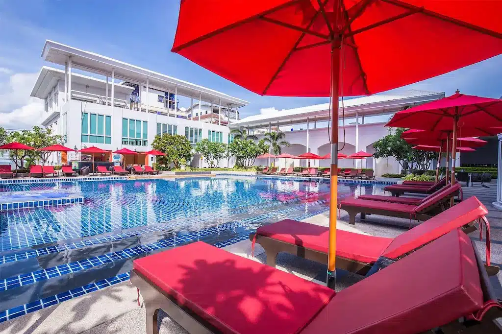 บริเวณสระว่ายน้ำกลางแจ้งของโรงแรมที่หาดจอมเทียนพร้อมเก้าอี้อาบแดดสีแดงและร่มในวันที่แดดจ้า ที่พักหาดจอมเทียน