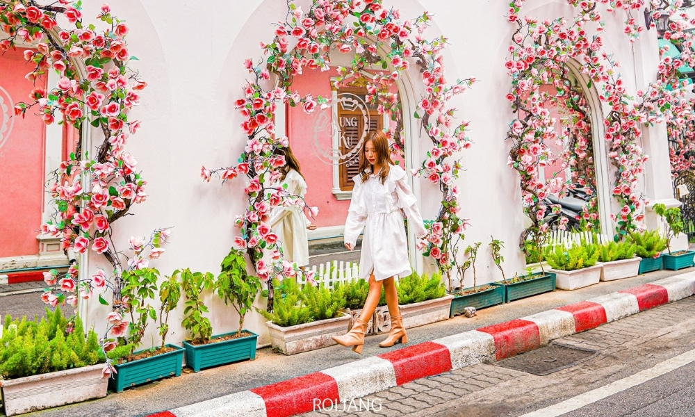 ผู้หญิงชุดขาวเดินผ่านหน้าร้านที่ประดับประดาด้วยดอกไม้หลากสีสันบน ถนนคนเดินภูเก็ต