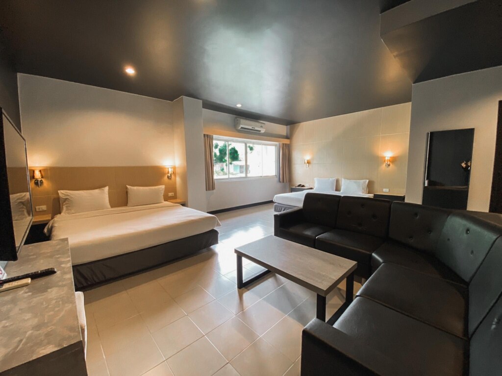 ห้องพักในโรงแรมทันสมัยพร้อมเตียงคิงไซส์ โคมไฟข้างเตียง พื้นที่นั่งเล่นพร้อมโซฟาสีดำ และโต๊ะกาแฟ ที่พักเบตง