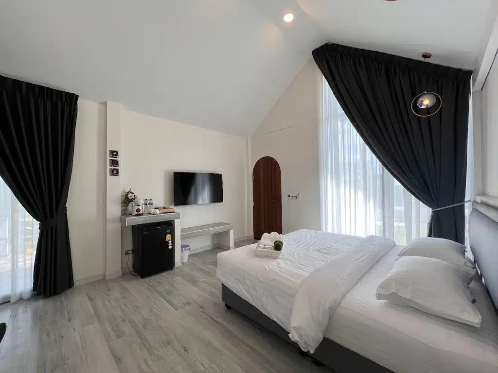 ห้องพักโรงแรมสไตล์โมเดิร์นโทนขาวดำ มีเตียงคู่ ทีวีติดผนัง หน้าต่างบานใหญ่พร้อมผ้าม่าน ที่ ที่พักเกาะแสมสาร