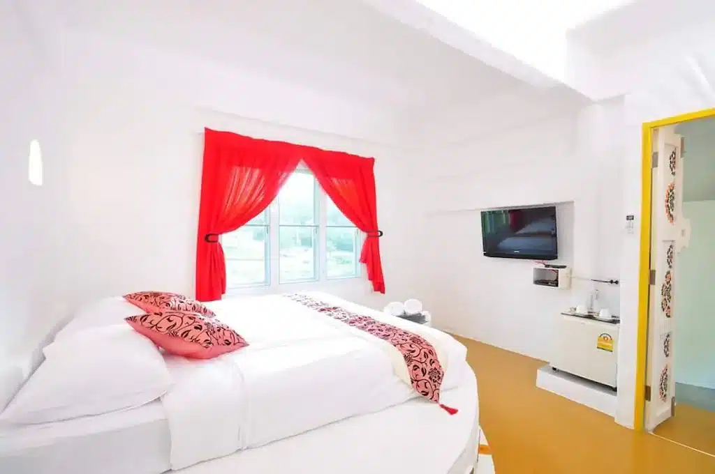 ห้องนอนสว่างสดใสทันสมัยผนังสีขาว เตียงคู่ตกแต่งด้วยสีแดง และทีวีจอแบนติดผนังในรีสอร์ท รีสอร์ทมวกเ ที่พักมวกเหล็กติดน้ำตก