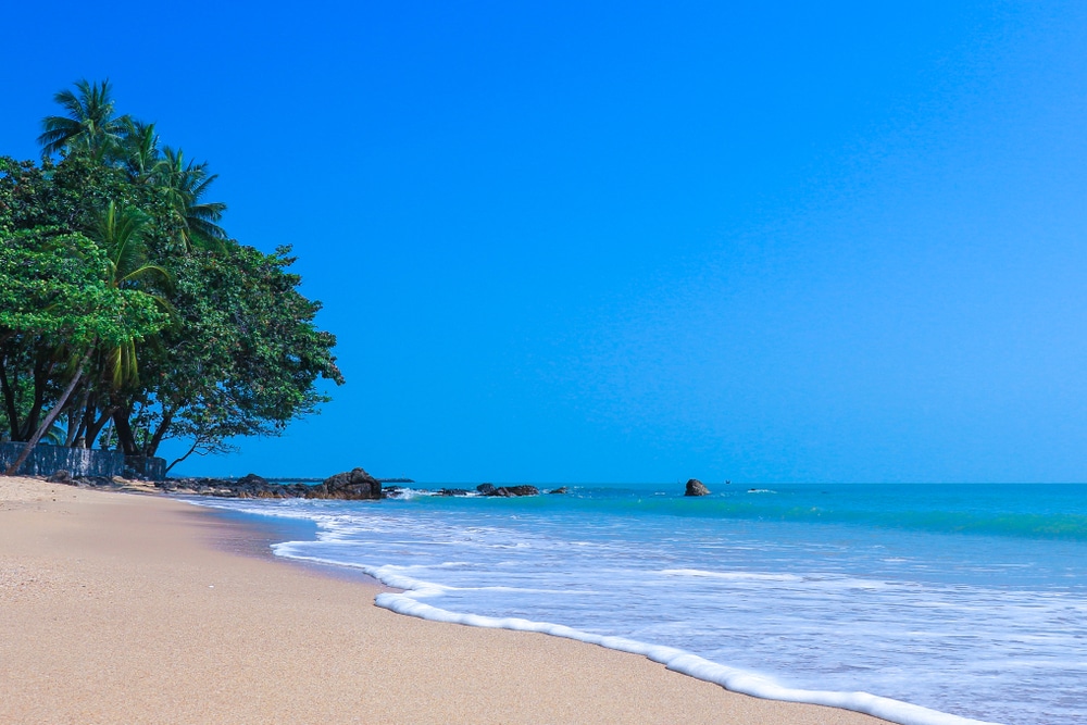 ชายหาดเขตร้อนที่มีท้องฟ้าสีฟ้าใส ต้นปาล์ม และคลื่นที่อ่อนโยน ที่เที่ยวนครศรีธรรมราช