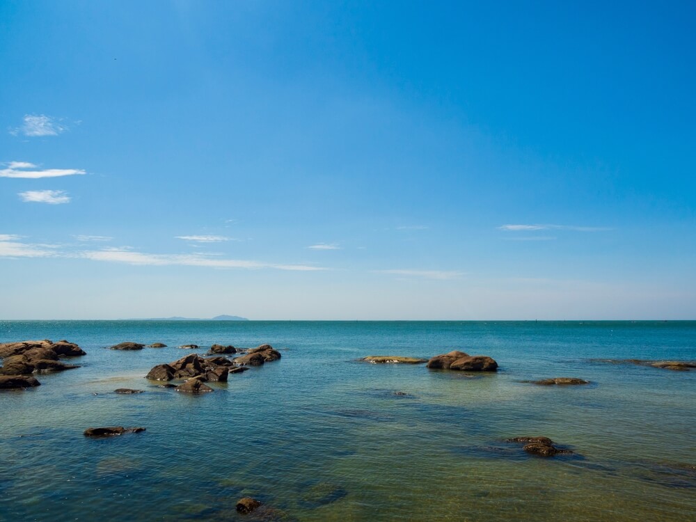 ชายหาดที่มีหินและน้ำภายใต้ท้องฟ้าสีคราม ทะเลสัตหีบ