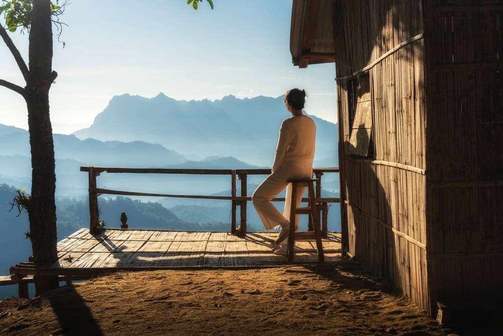 คนนั่งเงียบๆ บนระเบียงบ้านนาเลาใหม่ มองเห็นวิวภูเขายามพระอาทิตย์ขึ้น บ้านนาเลาใหม่