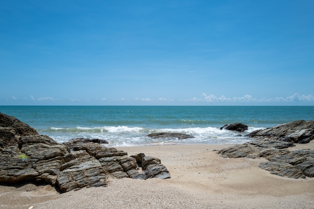 โขดหินโผล่ขึ้นมาบนหาดทรายพร้อมคลื่นทะเลใต้ท้องฟ้าสีฟ้าใส ที่เที่ยวขนอม