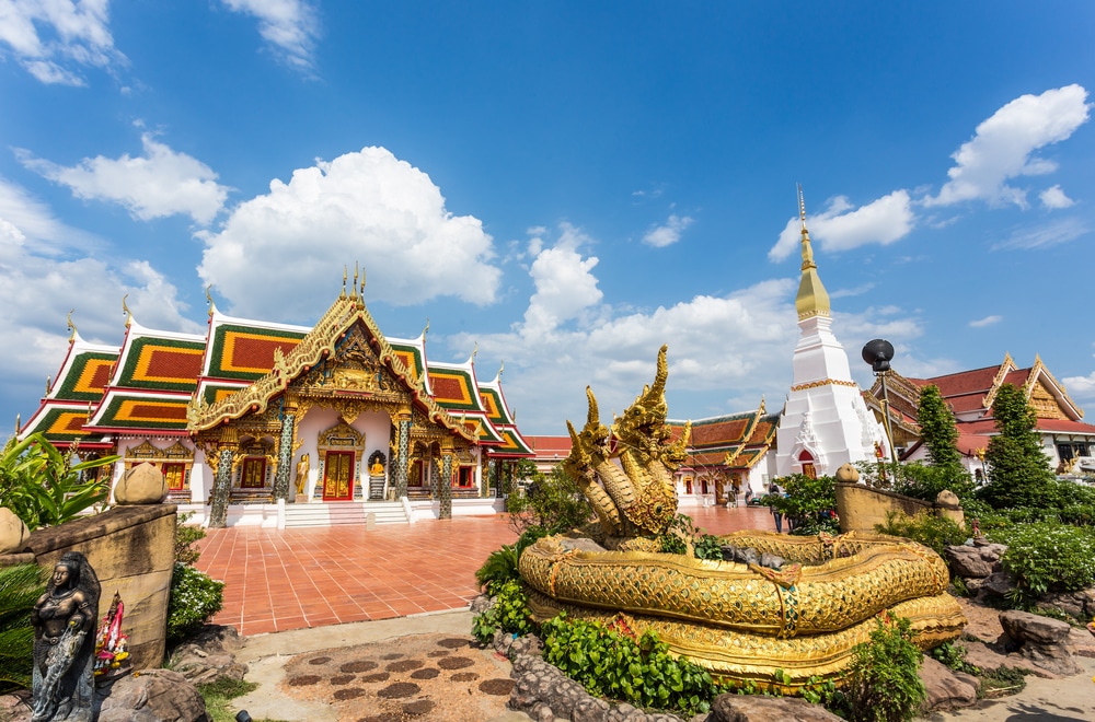 วัดไทยแบบดั้งเดิมที่มีอาคารอันวิจิตรงดงามและรูปปั้นสีทองใต้ท้องฟ้าสีครามสดใส สถานที่ท่องเที่ยวสกลนคร