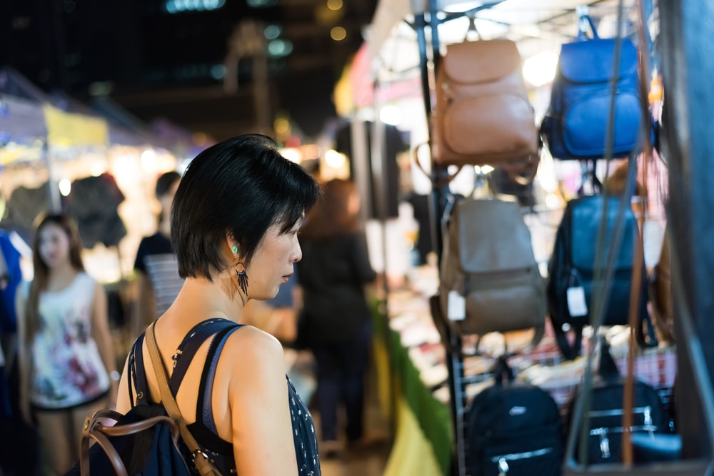 ผู้หญิงกำลังเดินดูกระเป๋าที่ตลาดบ้านเพ ตลาดนัดเลียบด่วนรามอินทรา