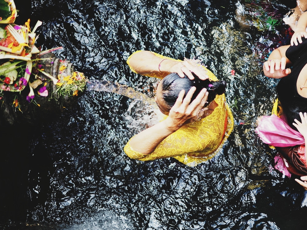 คนแต่งกายสีเหลืองกำลังอาบน้ำในแหล่งน้ำ อาจเป็นไปได้ในพิธีทางศาสนาหรือวัฒนธรรมที่ราชบุรี บาหลีที่เที่ยว