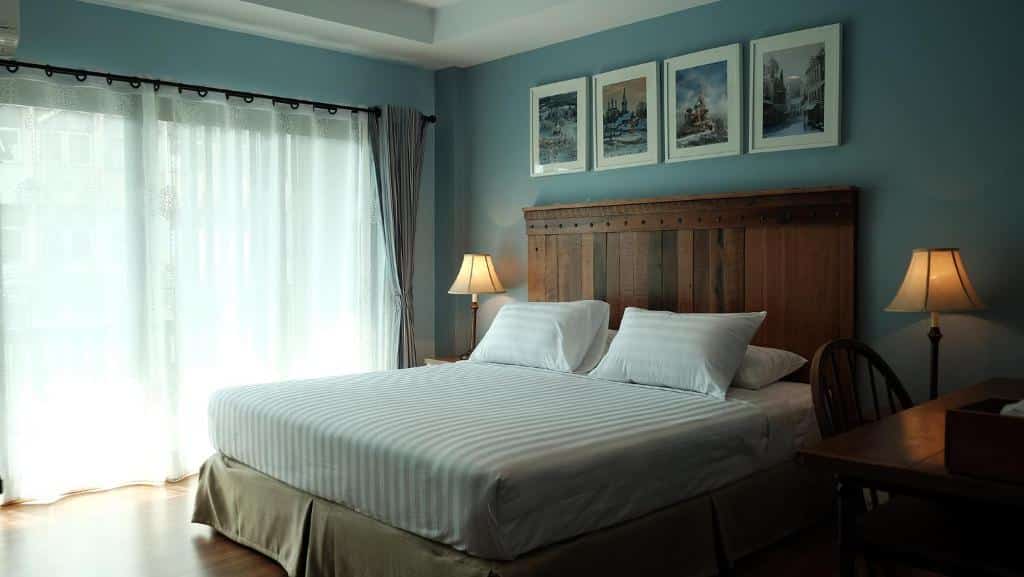 ห้องนอนแสนสบายพร้อมเตียงขนาดใหญ่ โคมไฟข้างเตียงสองดวง และกรอบรูปเหนือเตียง วางชิดผนังสีฟ้าอ่อน และหน้าต่างม่านโปร่งที่มองเห็นริมแม่น้ำในฉะเชิงเทรา ที่พักฉะเชิงเทราริมน้ำ
