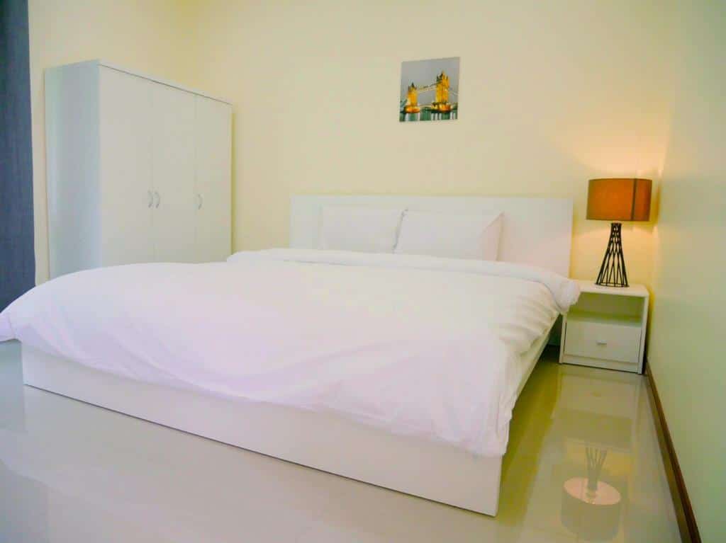 ห้องนอนสไตล์โมเดิร์นมินิมอลพร้อมเตียงสีขาวขนาดใหญ่ ตู้เสื้อผ้าสีขาว และโต๊ะข้าง ที่พักฉะเชิงเทราริมน้ำ เตียงขนาดเล็กพร้อมโคมไฟ ภาพวาดเล็กๆ แขวนอยู่เหนือเตียงในที่พักริมแม่น้ำในจังหวัดฉะเชิงเทราแห่งนี้