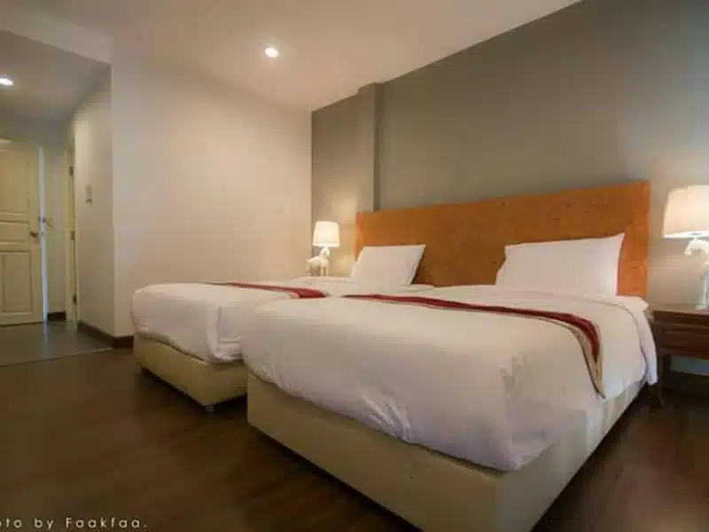 ห้องพักในโรงแรมที่มีแสงสว่างเพียงพอพร้อมเตียงแฝด 2 เตียง ผ้าปูที่นอนสีขาว และหัวเตียงตกแต่งด้วยสีส้มน้ำตกขุนกรณ์เชียงราย  ธีมน้ำตกขุนกรณ์เช