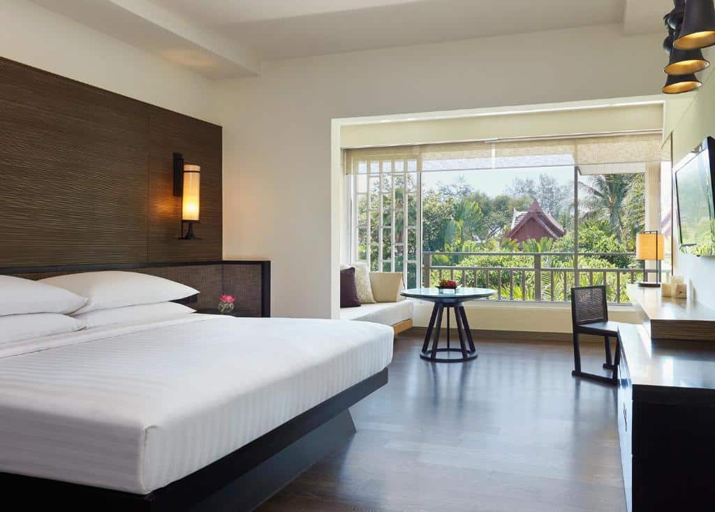 ห้องพักโรงแรมทันสมัยพร้อมเตียงขนาดใหญ่ หัวเตียงไม้ วิวทิวทัศน์อันเขียวชอุ่มของต้นไม้เขียวขจี และศาลาด้านนอกผ่านหน้าต่างบานใหญ่ในโรงแรมห  ที่พักหัวหิน