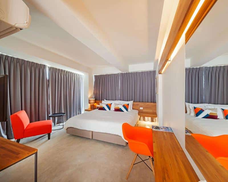 ห้องพักในโรงแรมทันสมัยในหัวหินที่มีเตียง 2 เตียงพร้อมชุดเครื่องนอนสีขาว เก้าอี้สีส้ม เฟอร์นิเจอร์ไม้ และไฟเพดานหรี่แสงได้  ที่พักหัวหิน