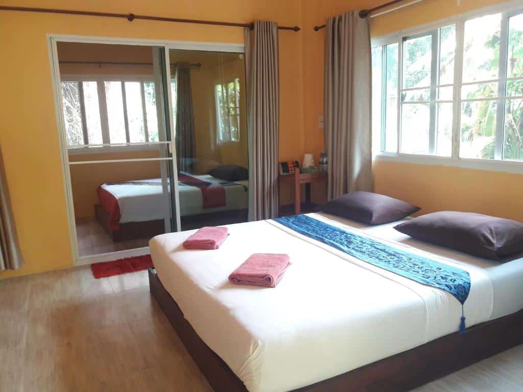 ห้องนอนสว่างสดใสกว้างขวางพร้อมเตียงขนาดใหญ่ ตู้เสื้อผ้ากระจก และพื้นไม้ที่ The Blue Sky Resort Ko Phayam มองเห็นความเขียวขจีผ่านหน้าต่างบานใหญ่ ที่พักเกาะพยาม