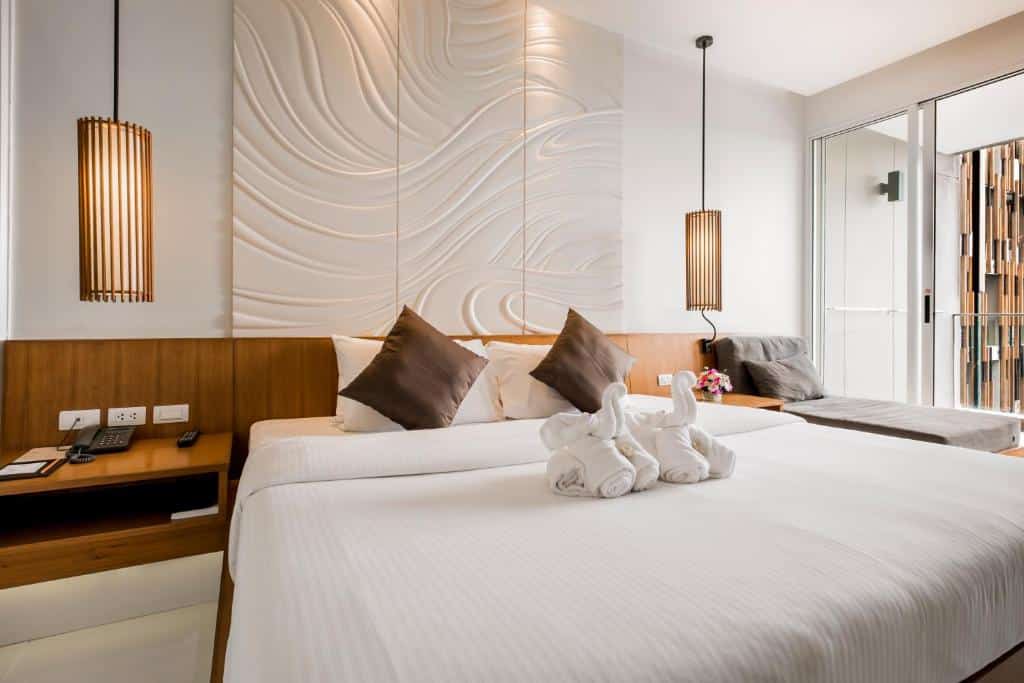 ห้องพักในโรงแรมทันสมัยในหัวหินที่มีเตียงขนาดใหญ่พร้อมผ้าปูที่นอนสีขาว หัวเตียงไม้ แผงตกแต่งผนัง หัวหินที่พัก และแสงไฟโดยรอบ