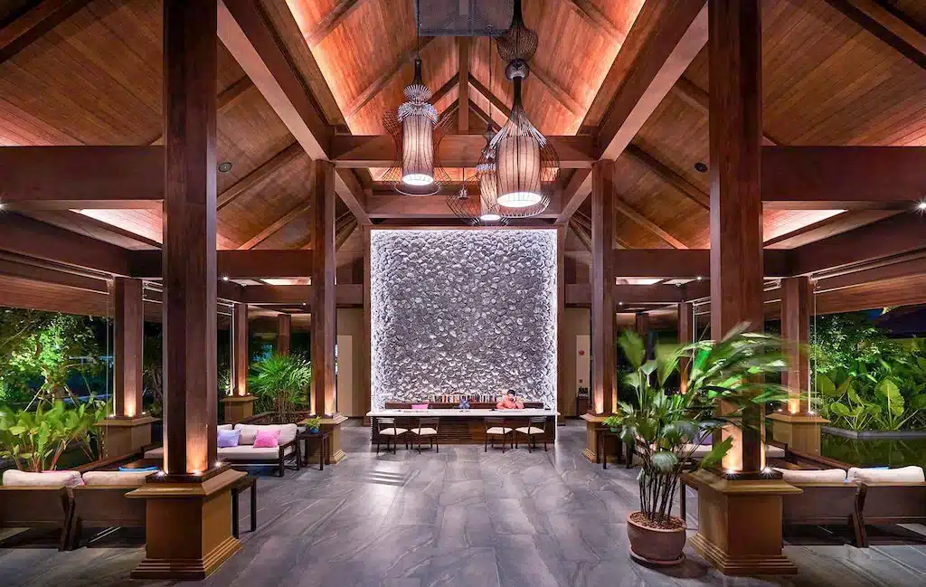 ล็อบบี้โรงแรมหรูสไตล์ทรอปิคอลพร้อมเพดานไม้สูง งานศิลปะจากหินตรงกลาง เฟอร์นิเจอร์หรูหรา และต้นไม้ในร่มอันเขียวชอุ่มในขนอม ที่พักขนอม