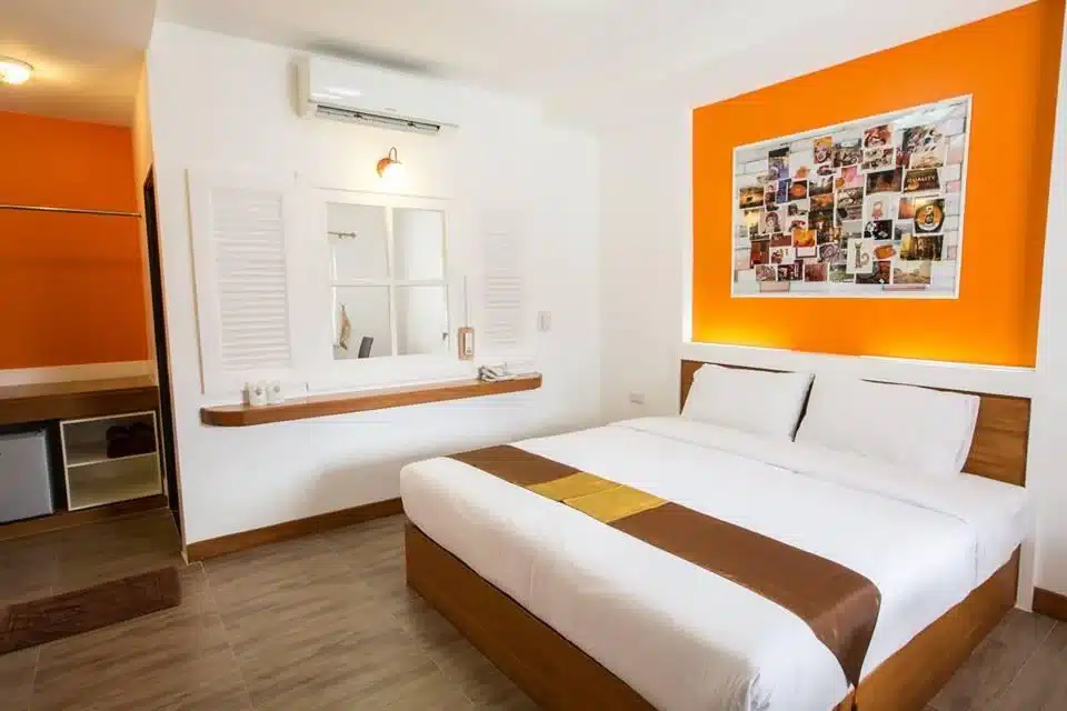 ห้องพักโรงแรมชัยนาทที่ทันสมัยและสว่างสดใสพร้อมผนังสีขาว เตียงขนาดใหญ่พร้อมผ้านวมสีแทนและสีทอง และเน้นสีส้มสดใส รวมถึง ที่พักชัยนาท