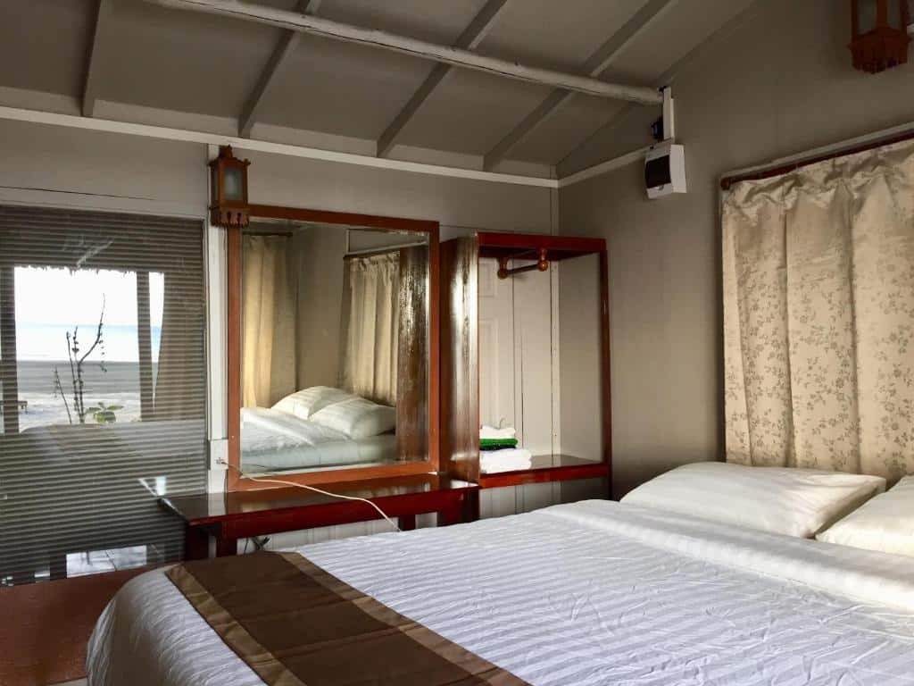 ภายในห้องนอนทันสมัยที่มีแสงสว่างเพียงพอที่เดอะบลูสกายรีสอร์ท เกาะพยาม พร้อมกระจกบานใหญ่ เตียงแฝด 2 เตียง และโต๊ะข้างกระจกในโทนสีกลางและสไตล์มินิมอล ที่พักเกาะพยาม