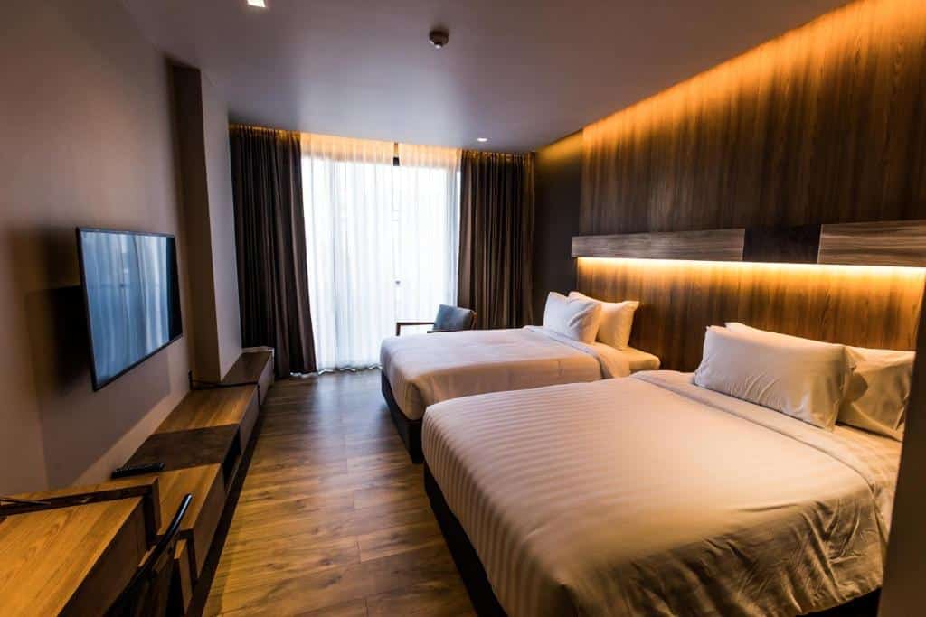ห้องพักในโรงแรมทันสมัยพร้อมเตียงแฝดสองเตียง หัวเตียงไม้ แสงไฟโดยรอบ ทีวีจอแบนบนผนัง และผ้าม่านโปร่งเหนือหน้าต่างพร้อมวิวดอยฮัด ดอยหัวหมด