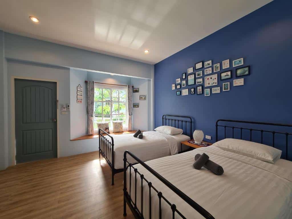 ห้องนอนผนังสีฟ้าสว่างสดใสพร้อมเตียงเดี่ยว 2 เตียง และผนังตกแต่งด้วยรูปภาพวัดพลวงในกรอบ เขาคิชฌกูฏ