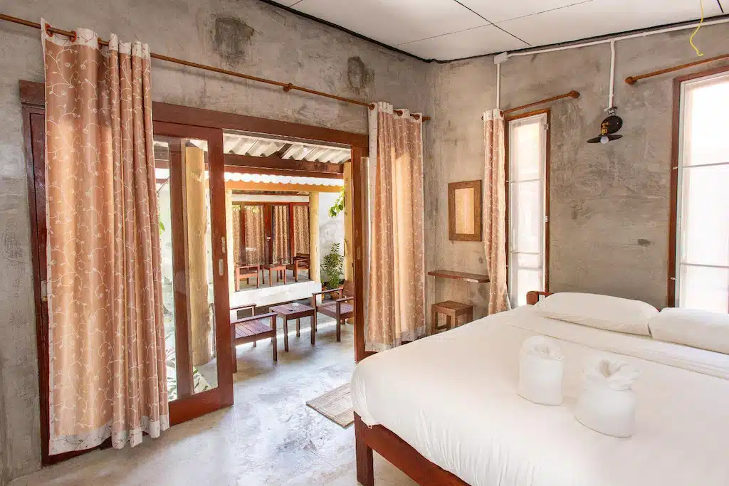 ห้องนอนเรียบง่ายที่บลูสกายรีสอร์ทเกาะพยามพร้อมเตียงขนาดใหญ่ ประตูระเบียงแบบเปิด ผ้าม่านโปร่ง คอนกรีต ที่พักเกาะพยาม