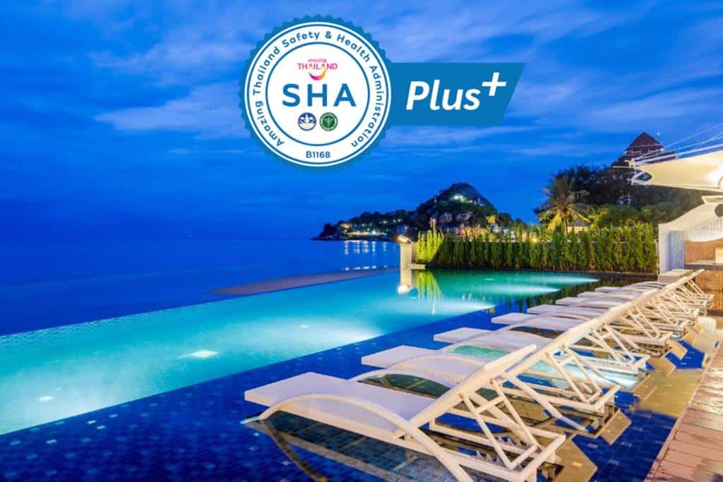 สระว่ายน้ำแบบอินฟินิตี้ที่มองเห็นทะเลในเวลาพลบค่ำพร้อมเก้าอี้นั่งเล่นเรียงรายอยู่บนดาดฟ้ากระเบื้อง โดยมีโลโก้  ที่พักหัวหิน "Thailand Safety and Health Administration SHA Plus" ที่ห้องอาหาร