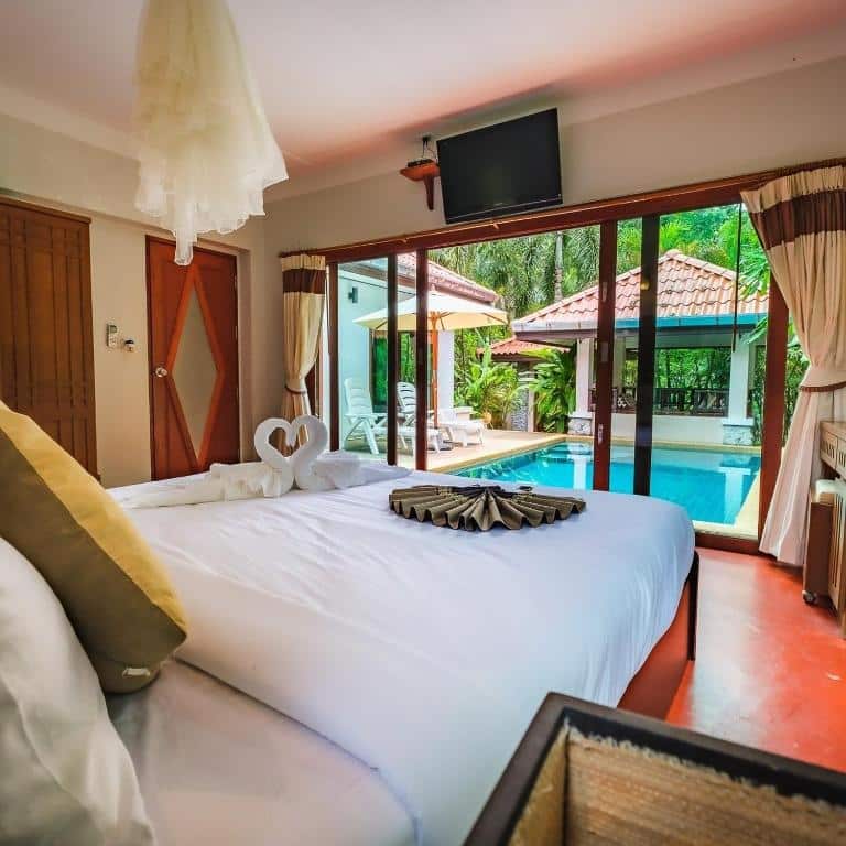 ห้องพักในโรงแรมแสนสบายพร้อมเตียงขนาดใหญ่ ทีวี และทางลงสู่สระว่ายน้ำส่วนตัวได้โดยตรง ล้อมรอบด้วยต้นไม้ ที่พักขนอม เขียวขจีในขนอม