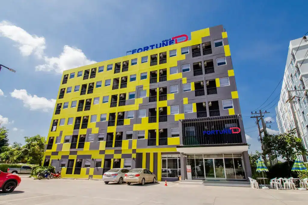 อาคารสำนักงานสไตล์โมเดิร์นที่มีส่วนหน้าอาคารสีเหลืองและสีเทาโดดเด่นภายใต้ท้องฟ้าสีฟ้าใส พร้อมโลโก้ "fortune d" ที่ด้านบน ที่พักตากคำขอแก้ไขของคุณเสร็จสมบูรณ์แล้ว:โรงแรมในตากที่มีความโดดเด่น