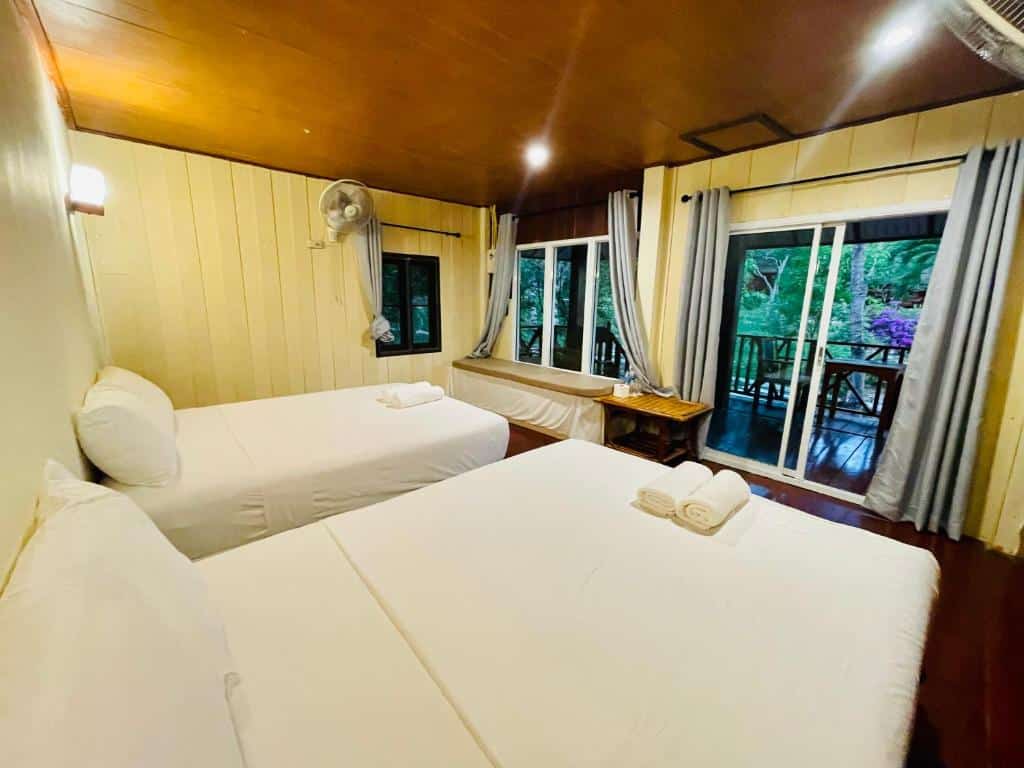 ที่พักเกาะพยาม ห้องนอนแสนสบายพร้อมเตียงเดี่ยว 2 เตียง ผนังไม้ และหน้าต่างบานใหญ่ที่มองเห็นป่าไม้เขียวชอุ่มที่เดอะบลูสกายรีสอร์ท เกาะพยาม