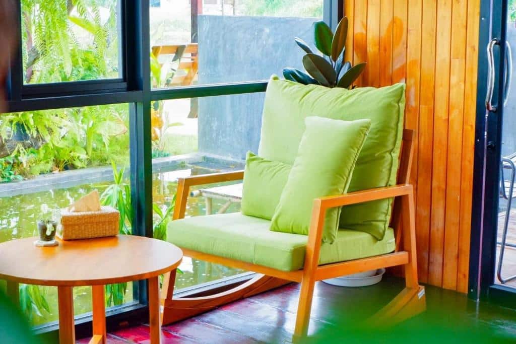 มุมสบายๆ กับเก้าอี้โยกเบาะสีเขียวริมหน้าต่างกระจกมองเห็นสวน คู่กับโต๊ะข้างไม้เล็กๆ ของ รีสอร์ทชัยนาท