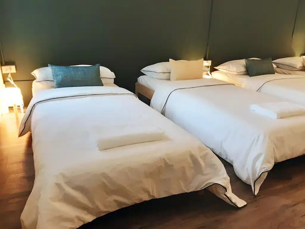 ห้องพักในโรงแรมทันสมัยพร้อมเตียงแฝดที่จัดสร้างอย่างประณีต 3 เตียง ผ้าปูที่นอนสีขาว และผนังสีเขียว  หาดเตยงามที่พัก สว่างไสวด้วยแสงอันนุ่มนวลที่หาดเตยงาม