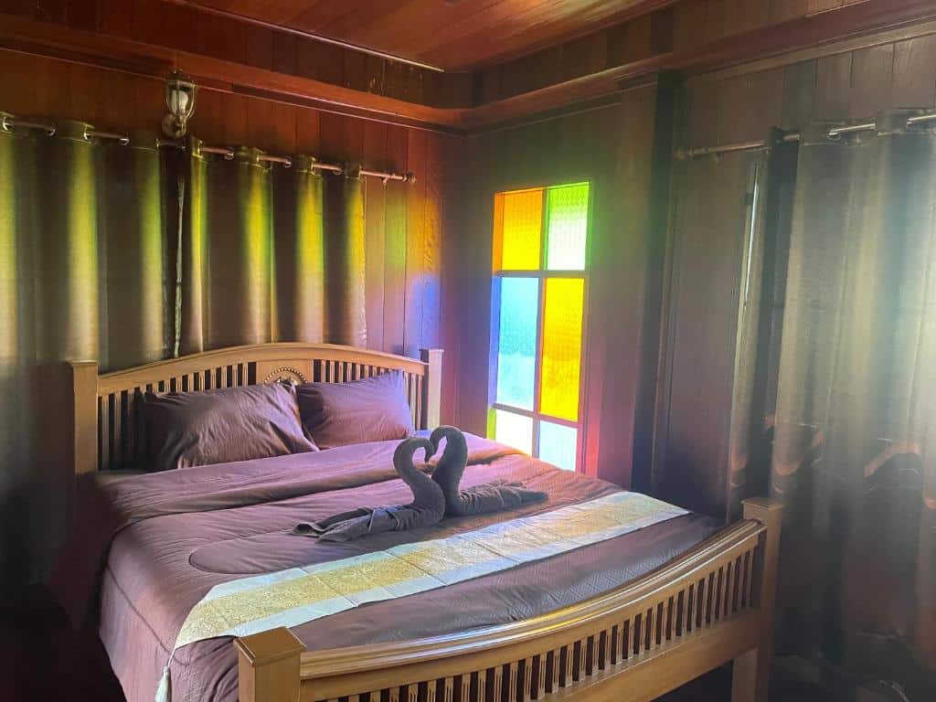เตียงที่จัดอย่างประณีตในห้องที่มีผนังไม้และหน้าต่างกระจกสีหลากสีสันที่ชัยนาทรีสอร์ท โดยมีแสงแดดลอดผ่านผ้าม่าน ที่พักชัยนาท