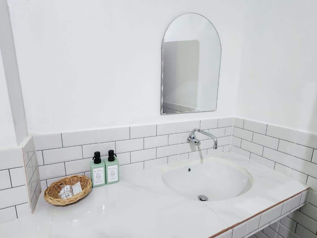 เคาน์เตอร์ห้องน้ำที่เรียบง่ายและสะอาดพร้อมอ่างล้างจาน กระจก และตะกร้าเล็กๆ ที่บรรจุของใช้ในห้องน้ำข้างขวดสองขวดที่ ชัยนาทรีสอร์ท ที่พักชัยนาท