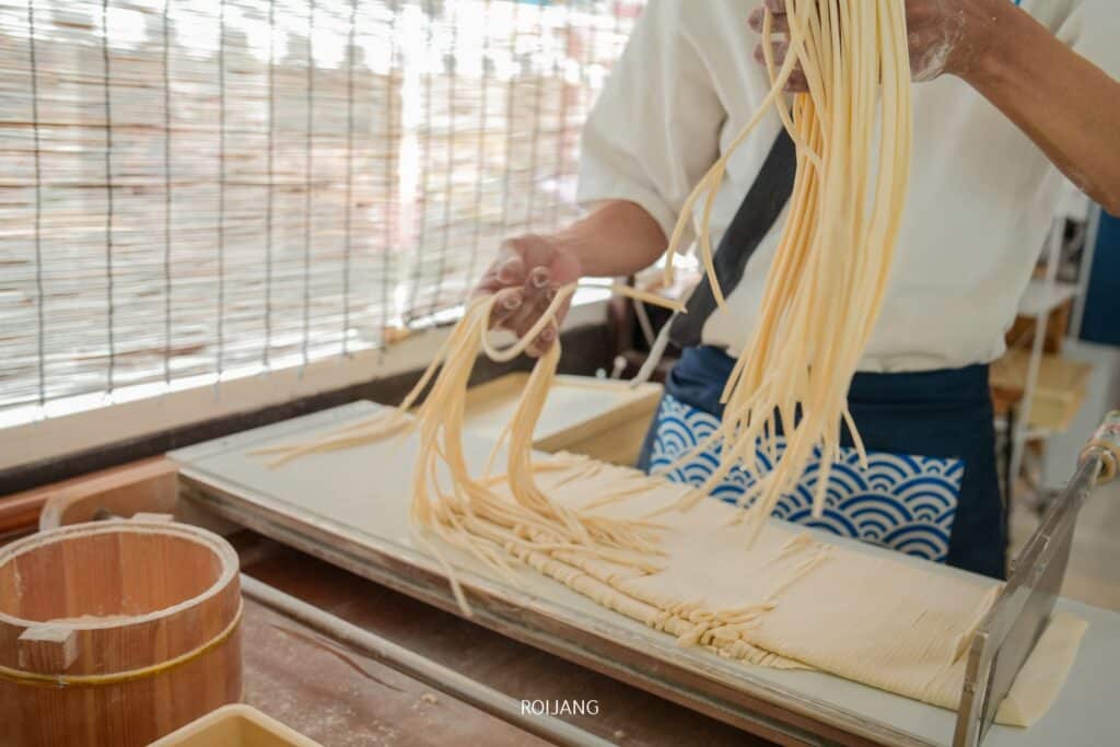 คนทำบะหมี่ด้วยมือ ยืดเส้นและวางจนแห้งบนถาดในเวิร์กช็อปที่มีแสงธรรมชาติกรองผ่านมู่ลี่ที่ร้านอาหารญี่ปุ่นในภูเก็ต  ร้านอาหารญี่ปุ่นภูเก็ต