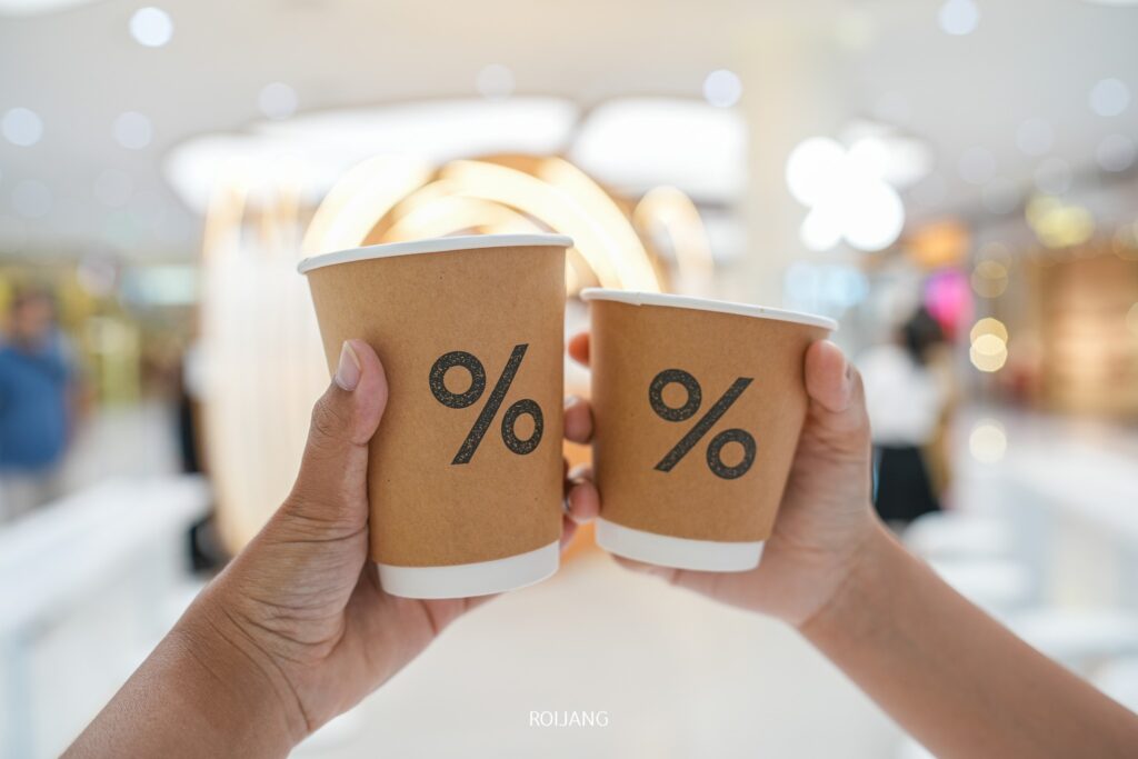 สองมือถือถ้วยกาแฟกระดาษพร้อมโลโก้สัญลักษณ์เปอร์เซ็นต์ ในร้านอาหารเซ็นทรัลภูเก็ตที่มีแสงสว่างจ้า