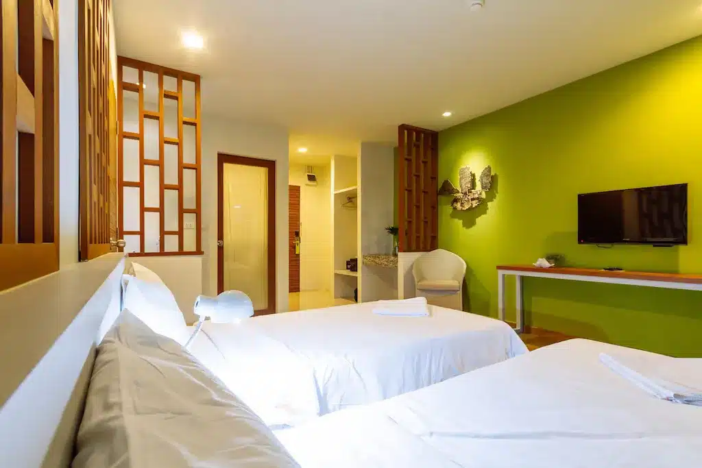 ห้องพักในโรงแรมทันสมัยและสว่างสดใสพร้อมเตียงแฝด ผนังสีเขียว ตกแต่งด้วยไม้ และโทรทัศน์แบบติดผนัง ทำหน้าที่เป็นเสน่ห์ดึงดูดใจใกล้กรุงเท ที่พักใกล้กรุงเทพ
