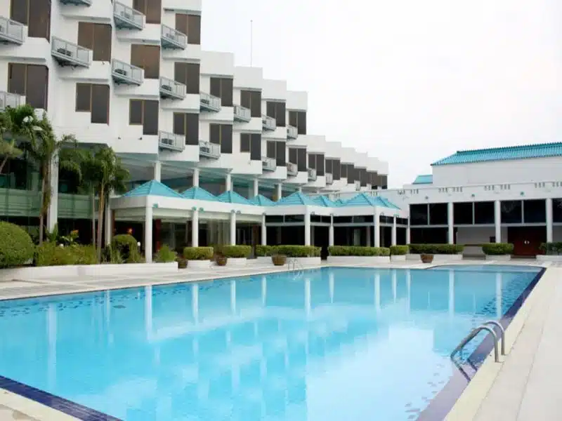 ที่พักฉะเชิงเทราริมน้ำ โรงแรมทันสมัยพร้อมสระว่ายน้ำขนาดใหญ่เบื้องหน้า ล้อมรอบด้วยอาคารสีขาวพร้อมกันสาดสีนกเป็ดน้ำ ตั้งอยู่ริมน้ำในจังหวัดฉะเชิงเทรา