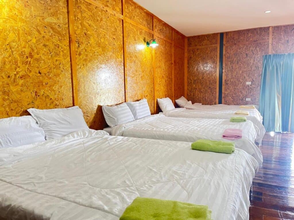 ห้องพักในโรงแรมที่เรียบง่ายพร้อมเตียงเดี่ยว 4 เตียง ผ้าปูที่นอนสีขาว และผนังกรุไม้ แสดงความสวยงามใกล้กรุงเทพ ที่พักใกล้กรุงเทพ