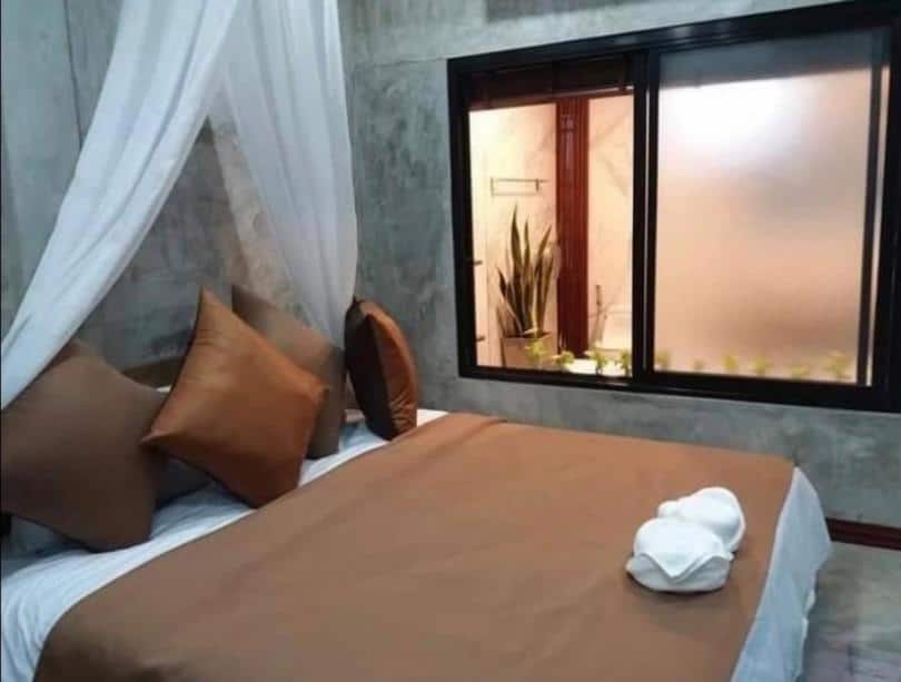 ห้องนอนที่ชัยนาทรีสอร์ทจัดอย่างประณีต มีผ้าคลุมเตียงสีน้ำตาล หมอนหลายใบ และผ้าเช็ดตัวสีขาวปูอยู่บนเตียง โรงแรมชัยนาท